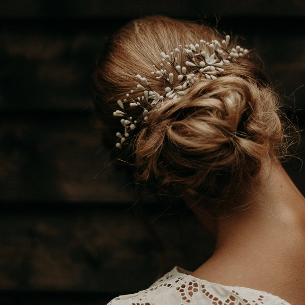 femme de dos avec un chignon bas et flou portant un accessoire de mariée en porcelaine, composé de fleurs et bourgeons légers