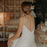 une femme de dos avec un chignon bas tressé,elle porte deux peignes un sur le coté gauche et un autre sur le coté droit en porcelaine mate