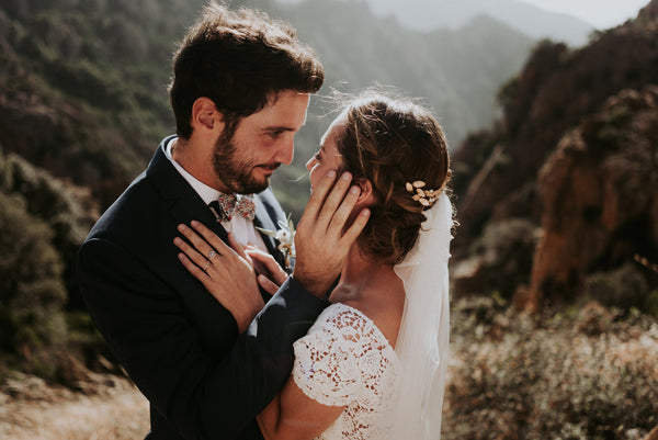 un couple de mariés en Corse se regardant dans la montagne. Elle porte unr robe lora Folk, un accessoire Lizeron, et un voile simple. Photo de Phan Tien
